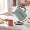 Green electric kettle pouring hot water into a mug for tea on kitchen counter