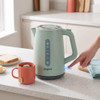 Green electric kettle on countertop, being switched on, next to mug with tea bag