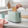 Hand removing crumb tray from green toaster to show easy cleaning feature