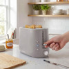 Grey 2-slice toaster with bread, hand pressing lever, kitchen counter setting