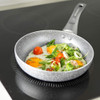 Grey non-stick frying pan with eggs, tomatoes and greens on induction hob