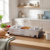 Buffet food warmer with three trays of roasted potatoes and mixed vegetables on kitchen worktop