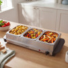 Stainless steel buffet server with three warming trays and clear lids, shown at angle.
