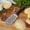 Stainless steel cheese grater with black handle shown with grated cheese and fresh herbs.