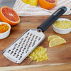 Stainless steel fine grater with black handle on chopping board with citrus zest and fruit