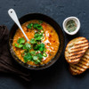 Bowl of lentil soup topped with fresh coriander and sliced chillies, served with toasted bread.