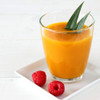 Glass of orange juice with two green leaves, served on a white plate with raspberries.