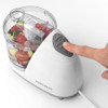 Electric food chopper with clear bowl, filled with avocado, onion and tomatoes, on kitchen counter.