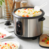 Stainless steel rice cooker with cooked rice and peppers on a kitchen worktop