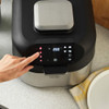 Hand pressing control panel on black and silver electric grill air fryer on kitchen counter