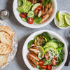 Grilled chicken salad with avocado, tomatoes, cucumber and lime in white bowl.