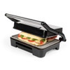 Black panini press toasting sandwich with tomato, cheese, and basil, lid partially closed