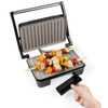 Grey electric grill with skewers of grilled chicken and vegetables, drip tray being removed