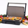 Electric grill with open lid, cooking chicken and vegetable skewers, surrounded by fresh vegetables