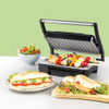 Contact grill with open lid, grilling skewers with vegetables, with salad and panini nearby