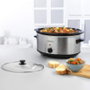 Progress stainless steel slow cooker filled with stew, lid off, beside bread and bowl