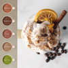 Mug of whipped cream-topped coffee with orange, cinnamon stick, coffee beans and flavour options.