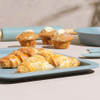 Almond croissants and muffins on blue bakeware, styled for kitchenware promotion