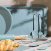 Set of blue baking utensils and tray, including whisk, spatula, and rolling pin, with croissants.