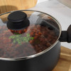 Black saucepan with glass lid showing tomato-based stew and parsley garnish.