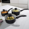 Set of non-stick grey saucepans and frying pans with glass lids, filled with assorted cooked food, shown top down.