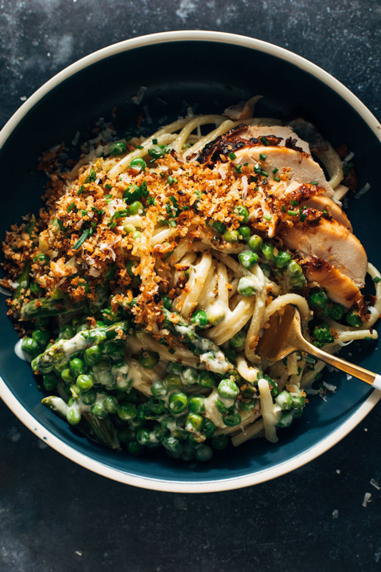 Bucatini pasta with peas, asparagus and chicken in a creamy cheesy sauces topped with breadcrumbs and served in a bowl