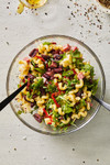 Pasta salad made with cavatappi pasta, olives, peppers, cheese and greens tossed in a glass serving bowl.