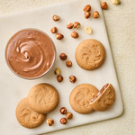 An overhead image of hazelnut cream filled cookies next to a bowl of hazelnut cream and hazelnuts.