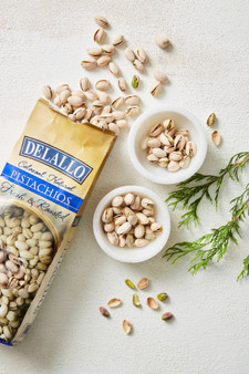 Bag of opened pistachios with two small bowls of pistachios.