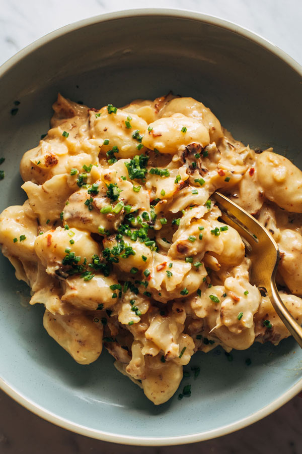 Gnocchi in a bowl tossed in a creamy orange sauce with cauliflower and chives.