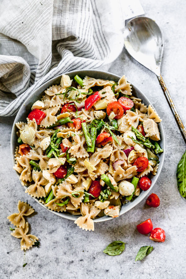 Pasta salad made with whole wheat farfalle pasta, asparagus, peppers, tomatoes and mozzarella balls tossed and served in a bowl