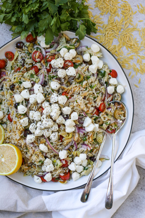 Orzo pasta tossed with tomatoes, olives, red onions and mozzarella cheese and served on a plate