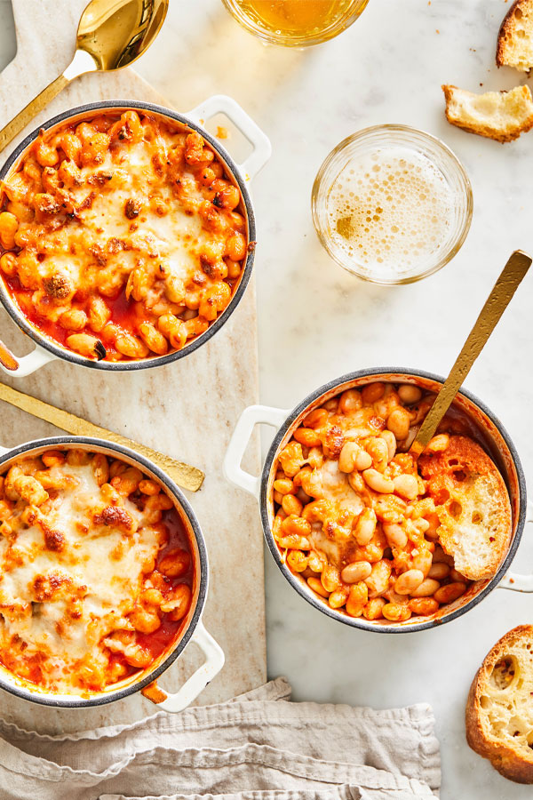 Mini dutch ovens filled with white beans, tomatoes, and melted cheese.