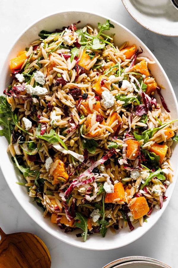 Orzo pasta tossed with butternut squash, pine nuts, goat cheese, radicchio and cranberries in a lemon balsamic dressing and served in a bowl.