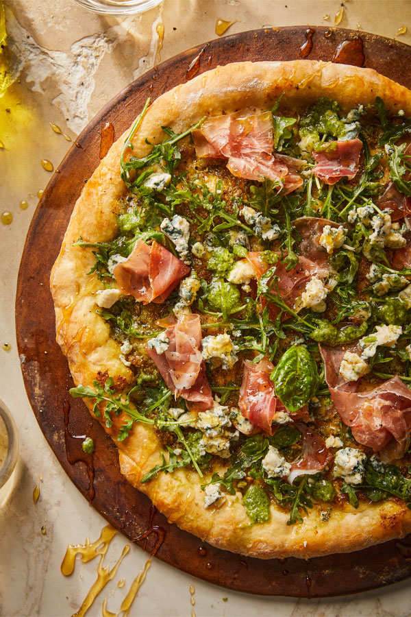 Pizza with pesto, prosciutto, and blue cheese.