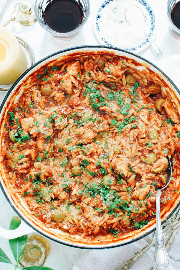 Orzo pasta in a pot with red sauce and green olives