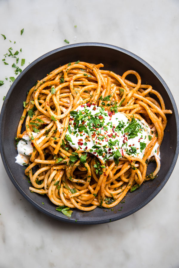 Bucatini pasta in a bowl tossed in a creamy red pepper sauce and topped with whipped feta cheese.