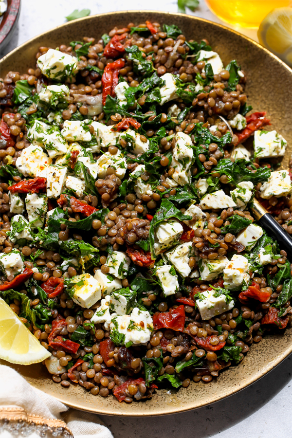 Cooked lentils in a salad with kale, sun-dried tomatoes, and marinated feta cheese.