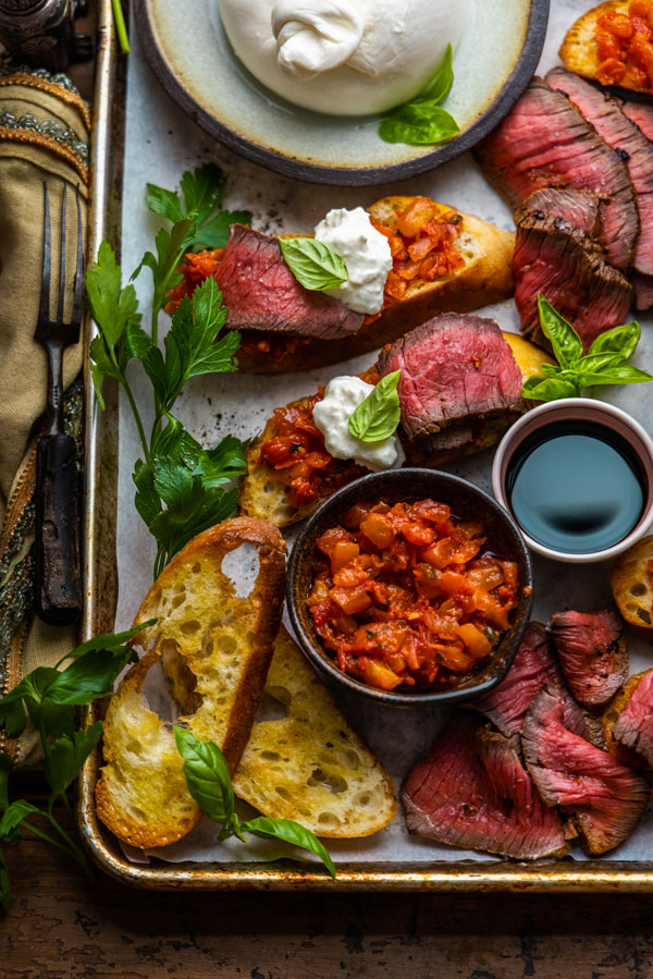 Steak and Burrata Crostinis displayed on a tray with Tomato Bruschetta