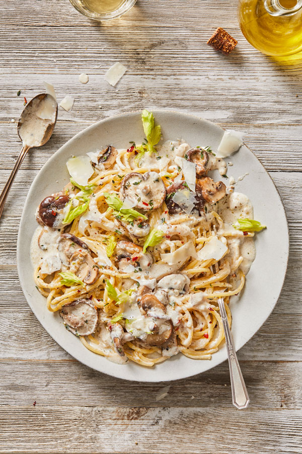 Bucatini pasta with mushrooms covered in a white cream sauce and topped with shredded parmesan cheese on a white plate.