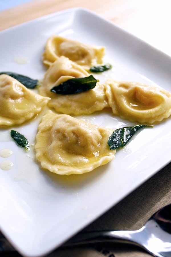 5 ravioli on a white plate with sage