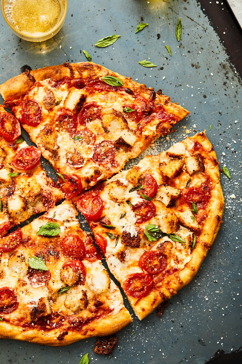 The pizza cut into slices being served on a table top. 