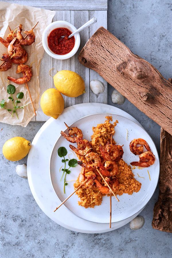 Creamy risotto topped with spicy pesto shrimp on white plate