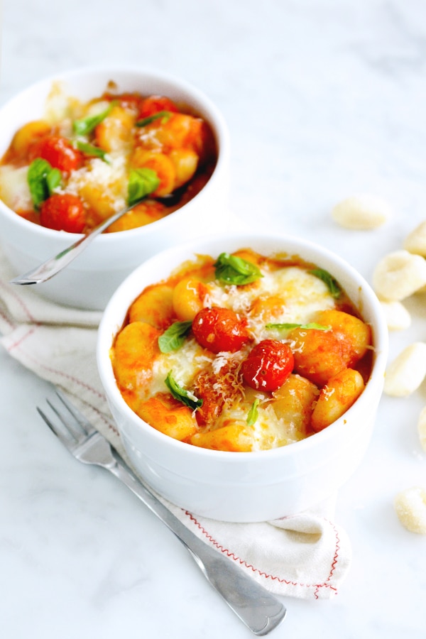 Two bowls of baked gnocchi topped with cheese and cherry tomatoes. 