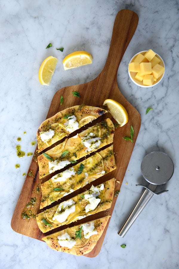 finished pizza topped with lemon, burrata cheese, and pesto - sliced on a wooden board