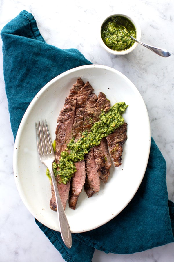 Flank steak topped with green sauce on white plate