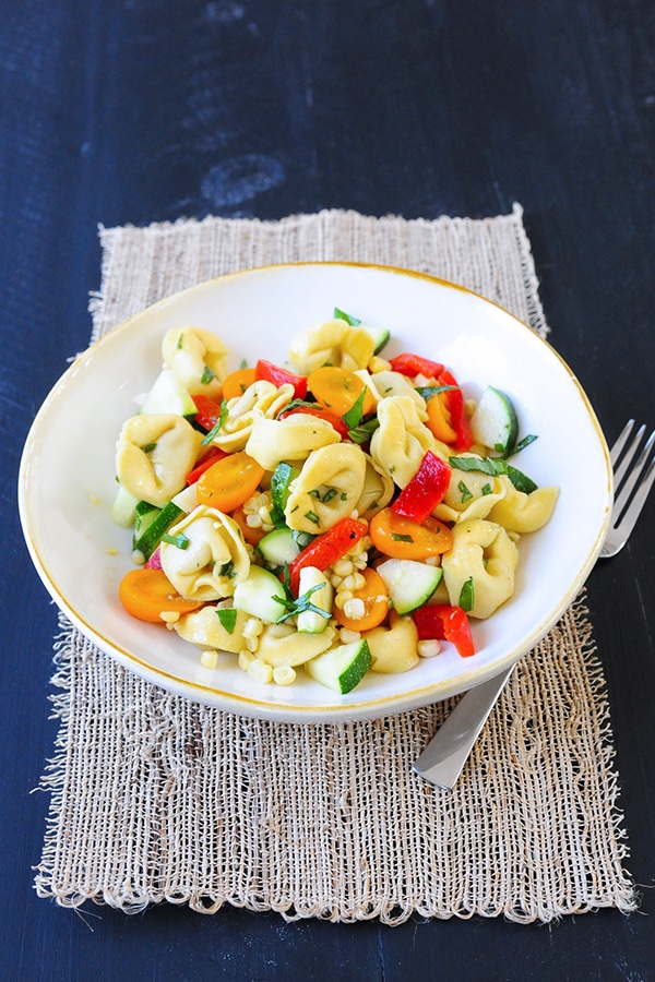 A shallow bowl served with tortellini, peppers, corn, zucchini and cherry tomatoes. 