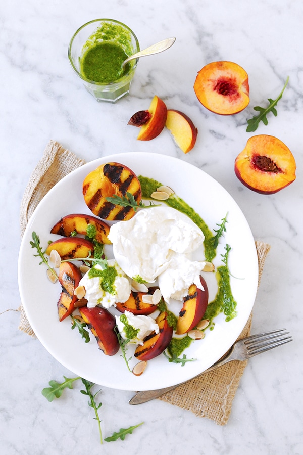 Grilled peaches served on a plate topped with burrata, arugula and pesto. 