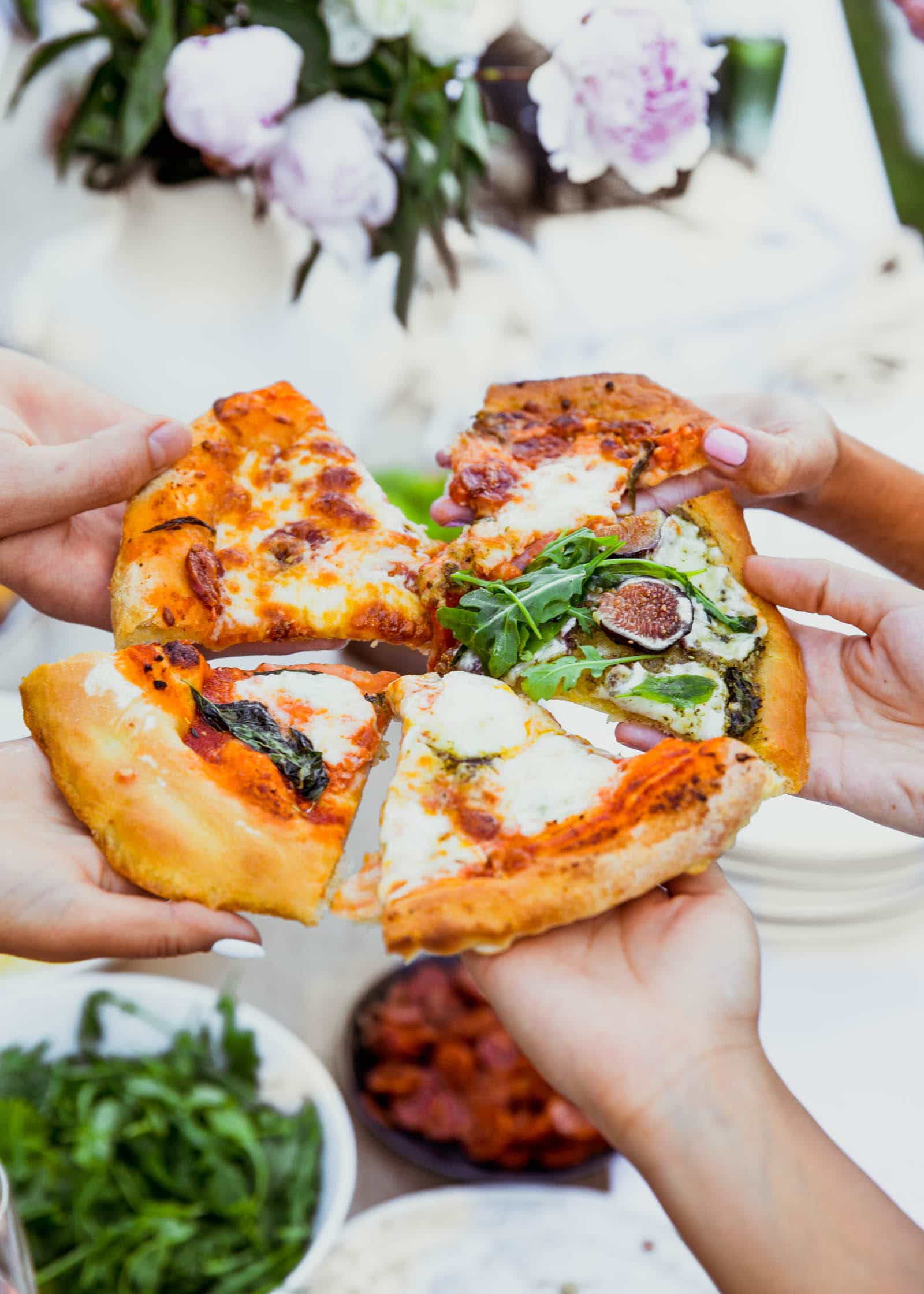 Five slices of pizza being held by different people ready to enjoy. 