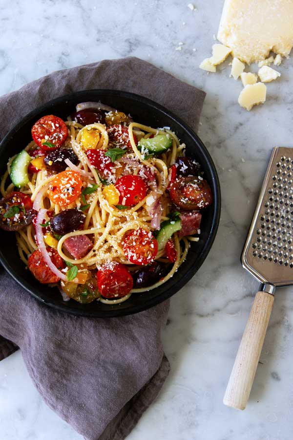 A skillet filled with spaghetti noodles, tomatoes, olives, cucumbers, onions and more. 